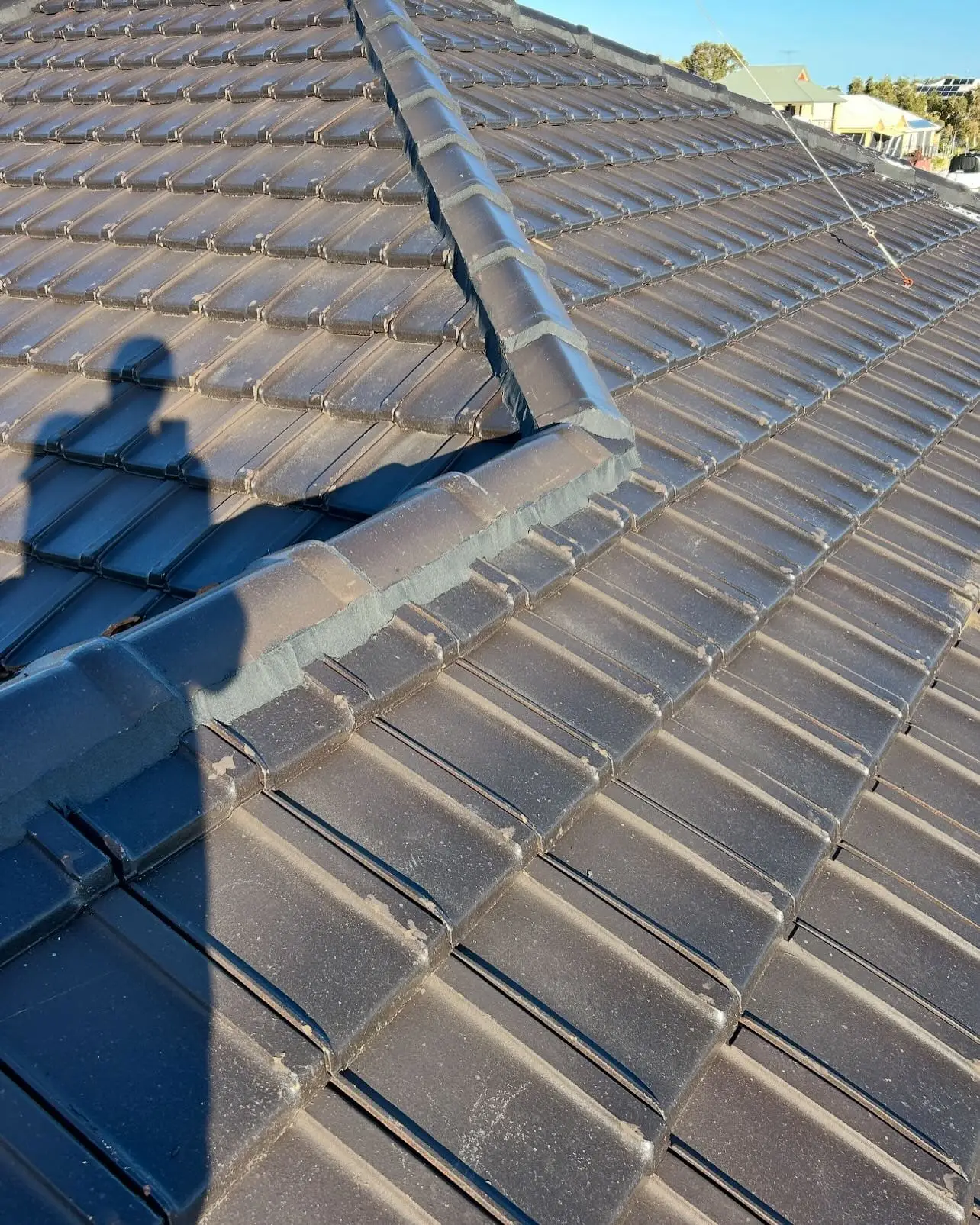 Roofer’s shadow across a repointed hip on a charcoal tiled roof