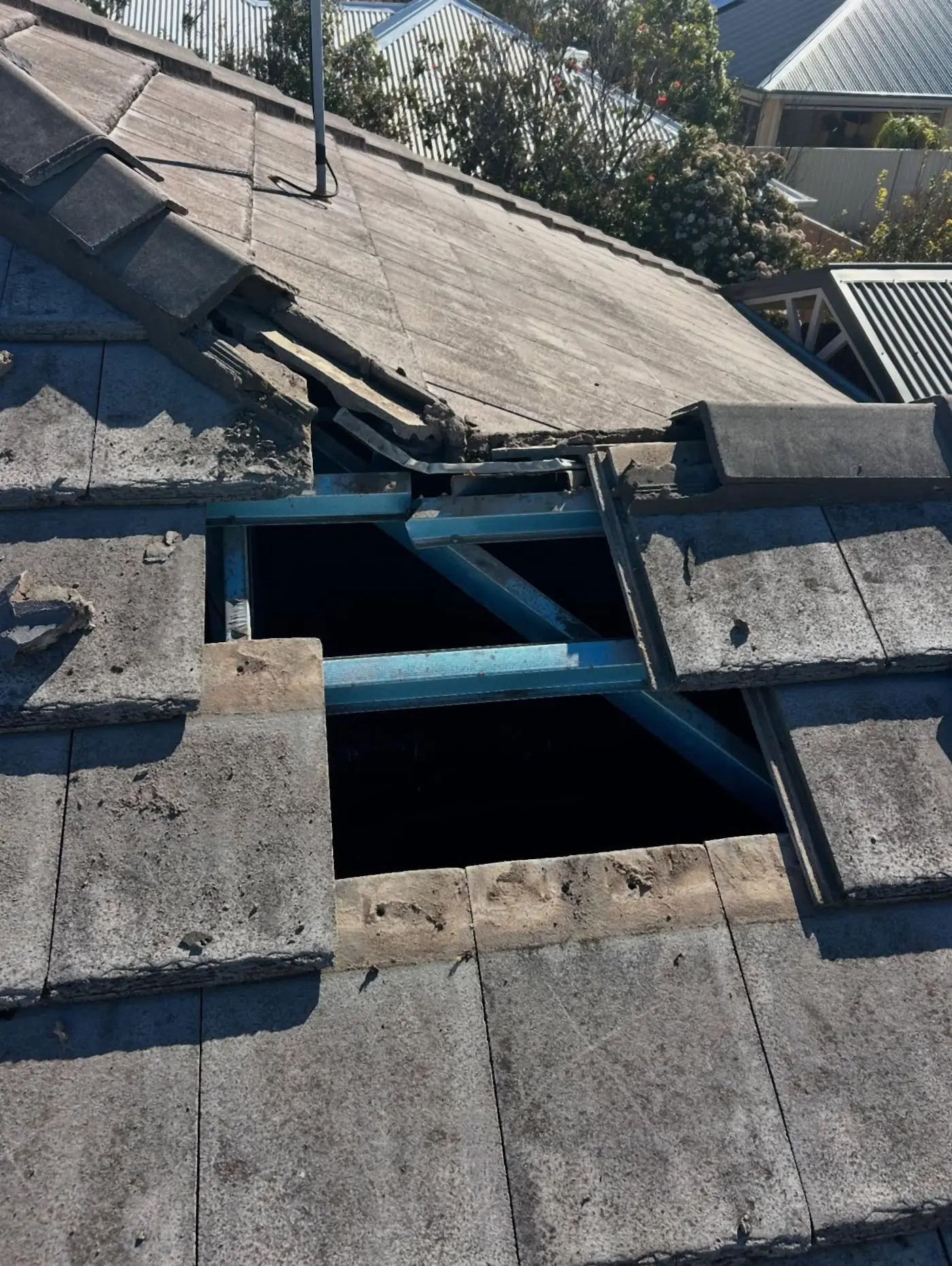 Grey concrete tiles lifted at the ridge to expose blue steel rafters
