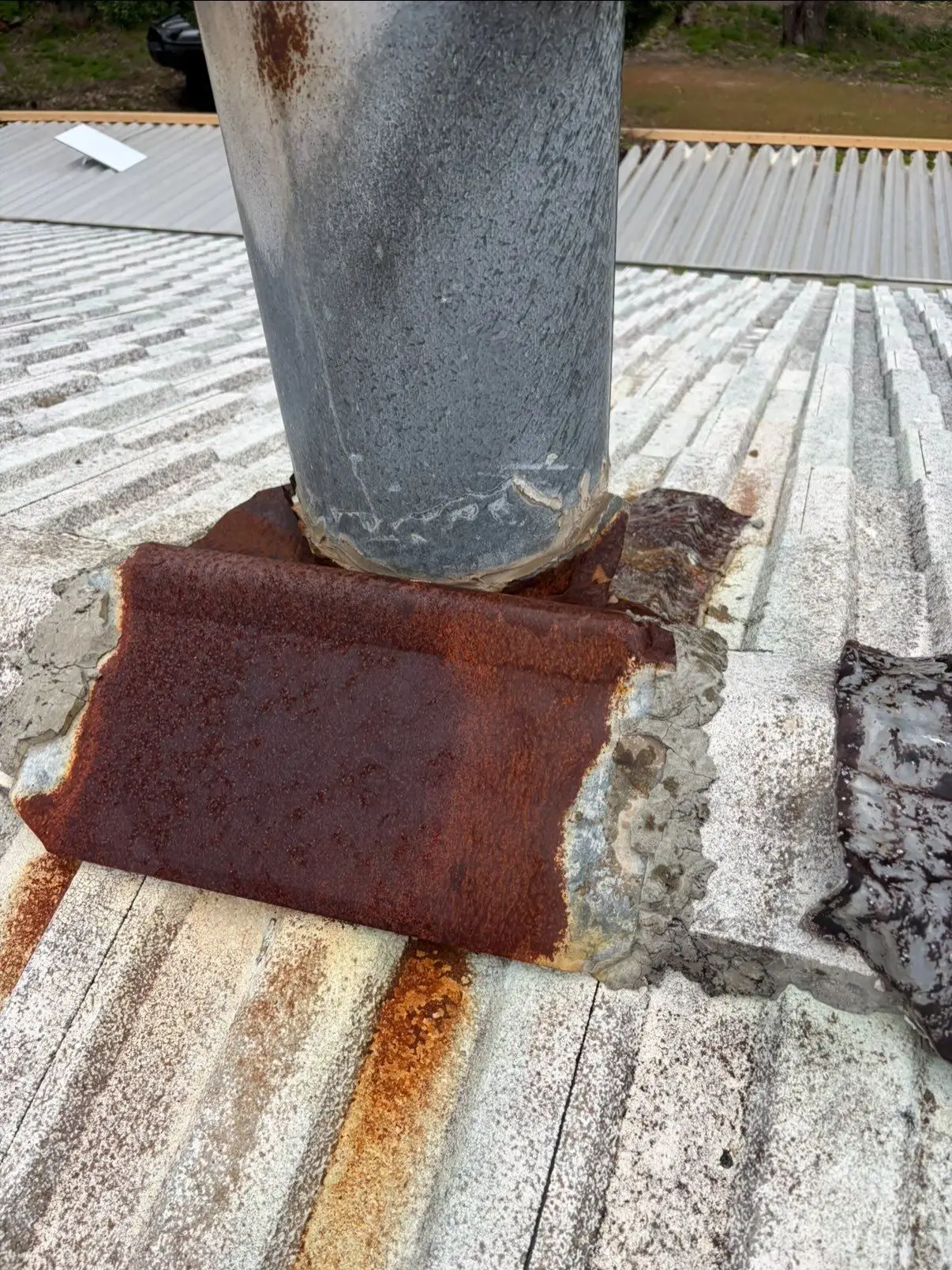 Old chimney flue with rusted flashing on a pale tiled roof