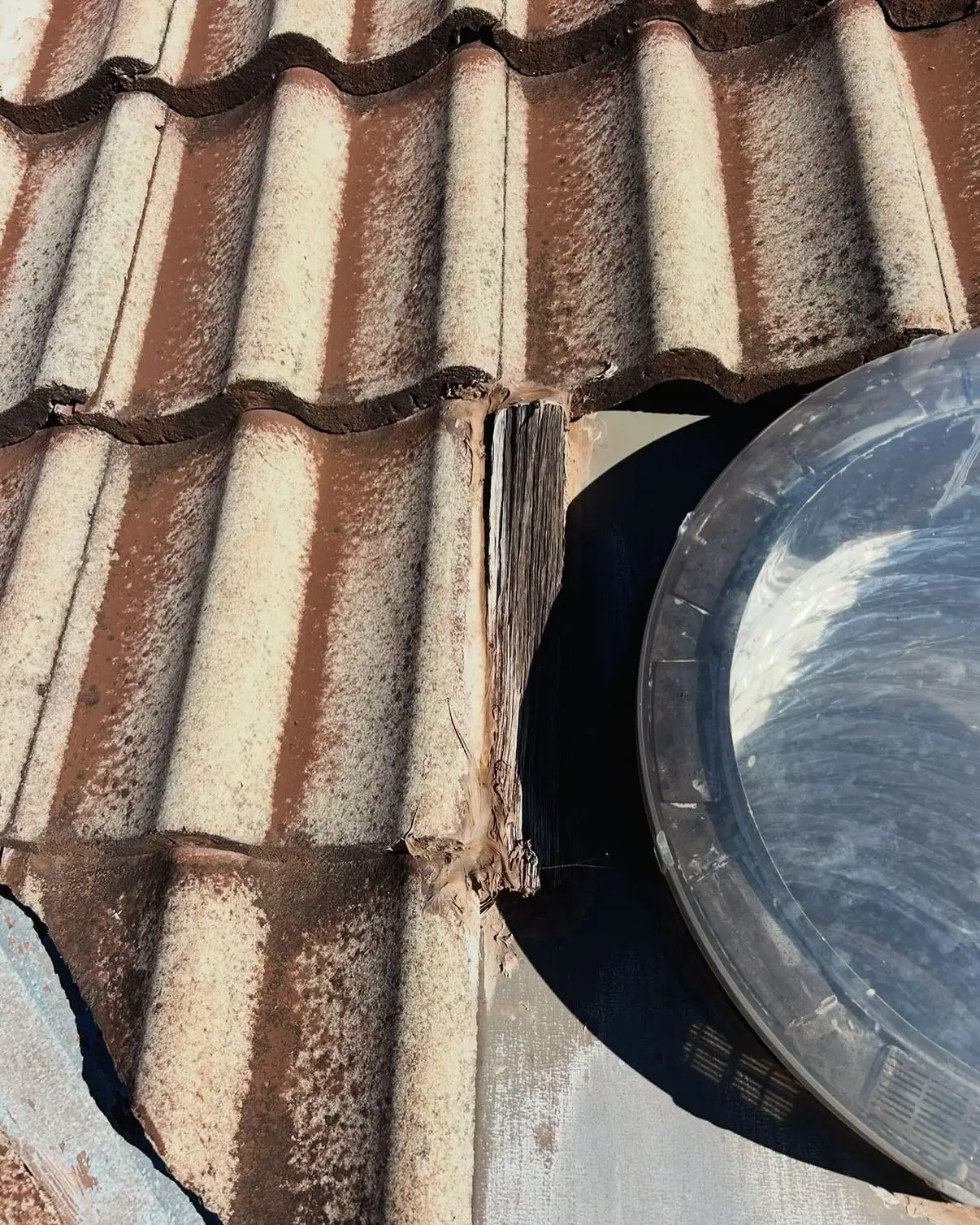 Tiles lifted beside a skylight dome on an older terracotta roof