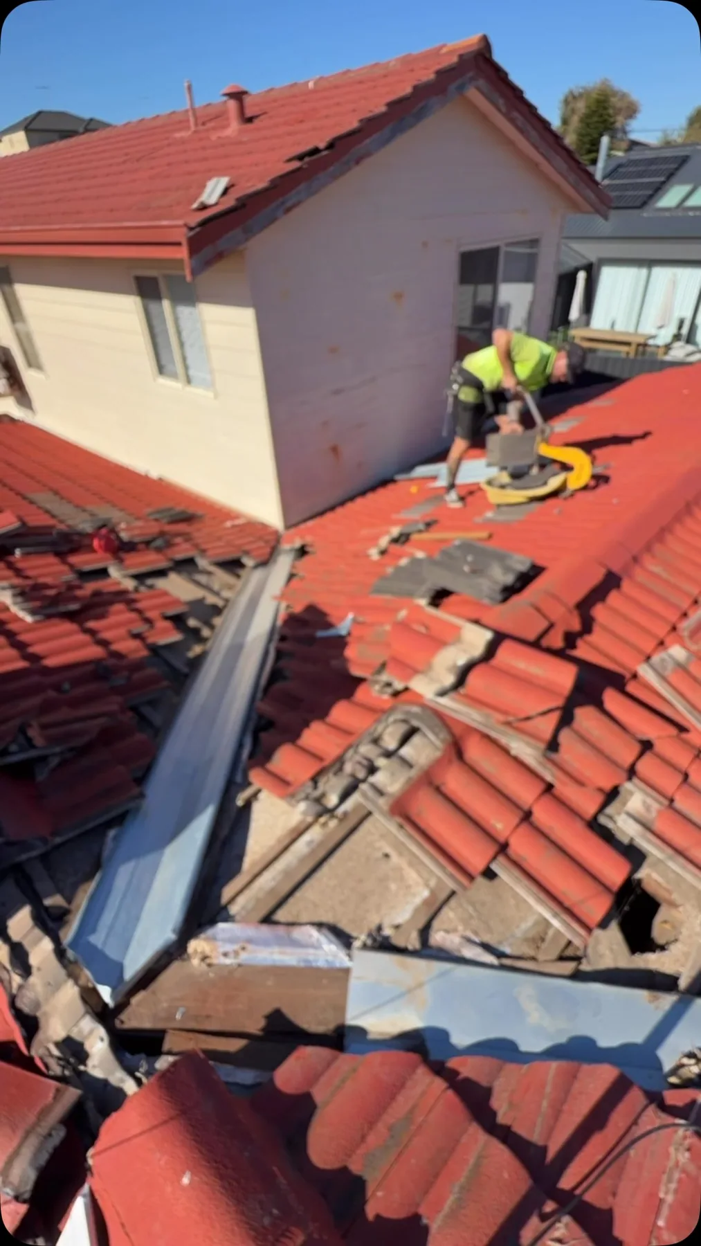 Roof tiles removed around a repair area with a roofer working beyond